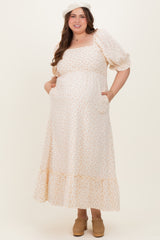 woman wearing a cream floral print maternity maxi dress with puff sleeves and pockets, showcasing a baby bump