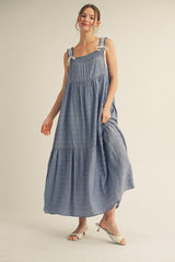 woman wearing a light blue sleeveless maxi dress with ruffled straps and a tiered skirt, standing against a neutral background