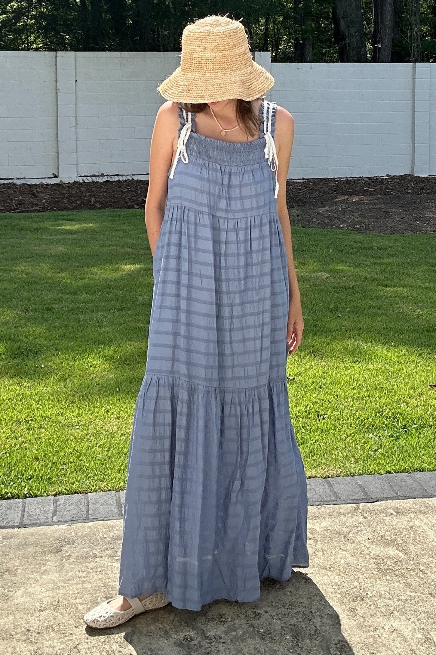 woman wearing a blue striped maxi dress with adjustable straps and a tiered skirt, standing in a grassy outdoor setting