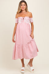 woman wearing a striped off-the-shoulder maternity dress with a ruffled hem and floral detail at the bodice