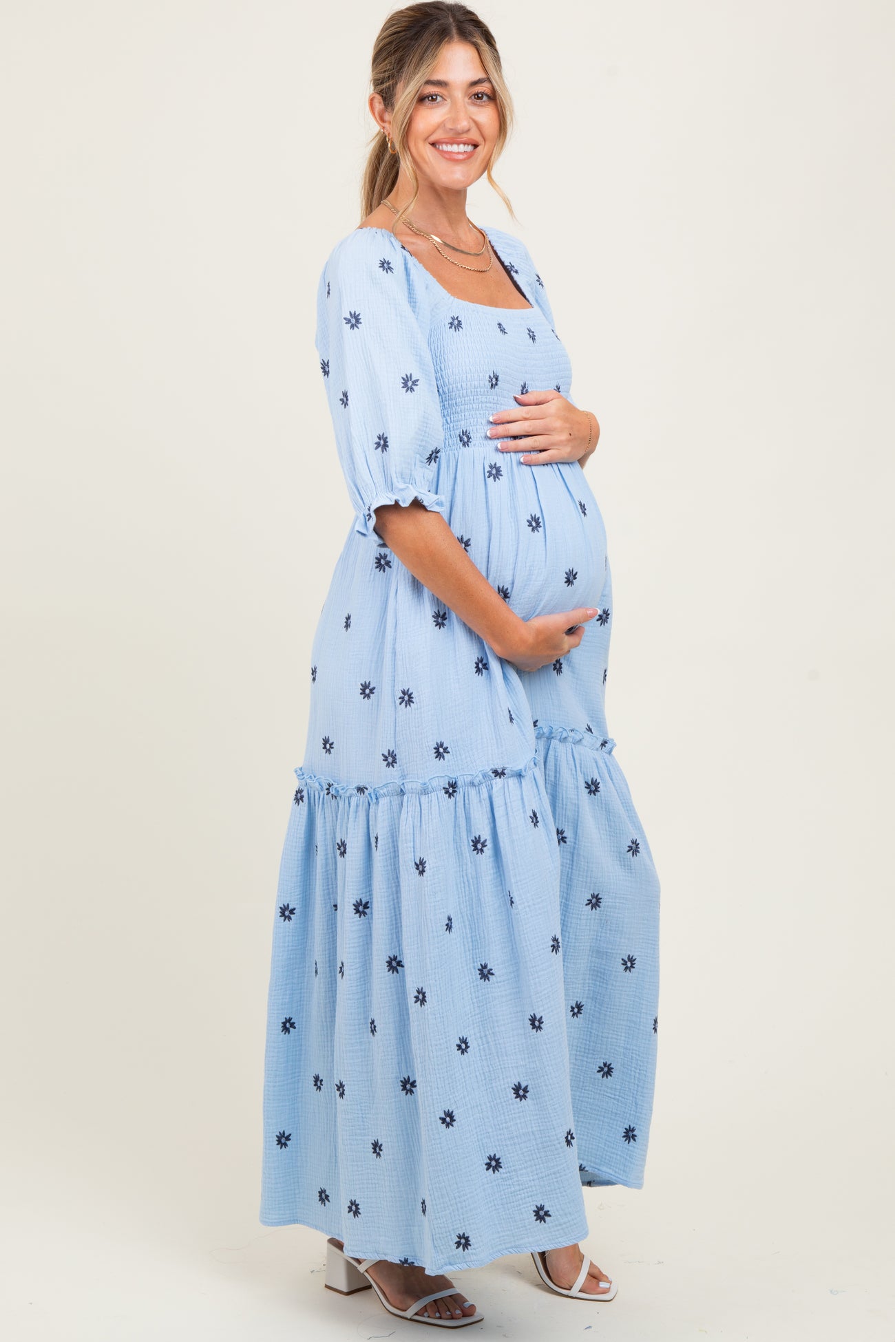 woman wearing a light blue maternity maxi dress with floral embroidery and a visible baby bump