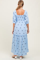 woman wearing a light blue maternity maxi dress with puff sleeves and floral embroidery on the back