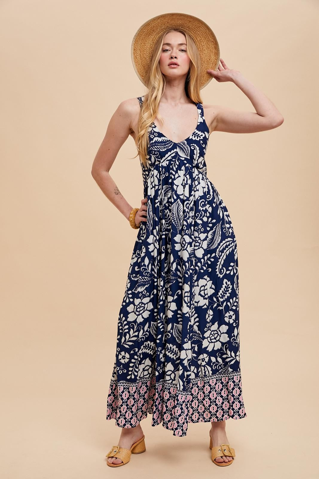 woman wearing a navy blue floral maxi dress with a v-neckline and a patterned hem, paired with a straw hat
