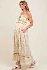 woman wearing a cream floral maternity maxi dress with adjustable straps and pockets, showcasing her baby bump