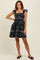 woman wearing a black floral print dress with ruffled sleeves and a tiered skirt, standing and smiling