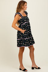 woman wearing a black floral print short dress with ruffled sleeves and pockets, standing sideways