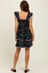 woman wearing a black floral print dress with ruffle sleeves and pink trim, view from the back