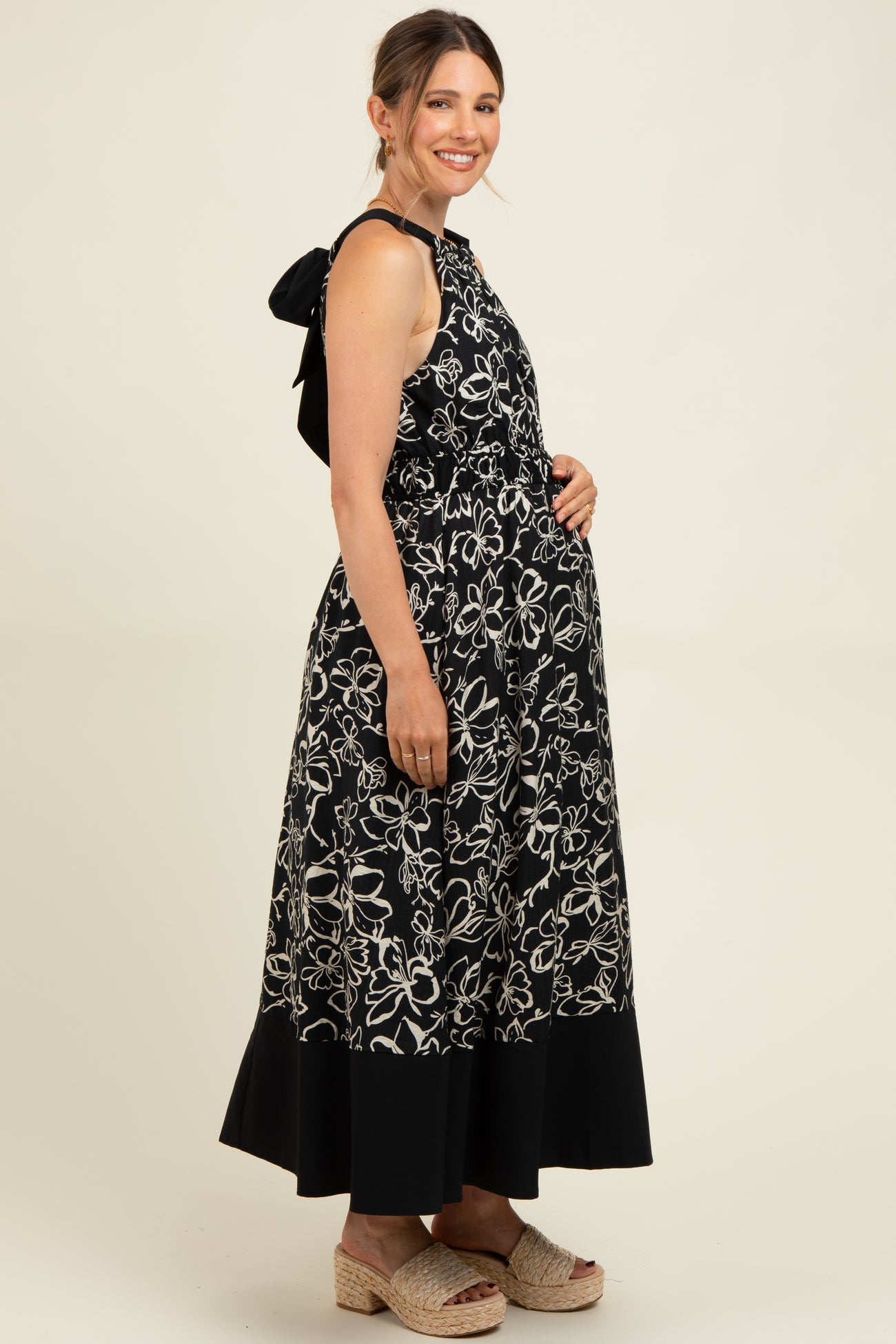 woman wearing a black floral maternity maxi dress with a tie-back detail and showing her baby bump