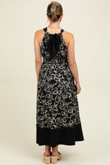 woman wearing a black maternity maxi dress with floral details and a tied back, showcasing a baby bump