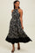 woman wearing a black floral maxi dress with a halter neckline and flowy skirt, smiling and posing while holding the hem