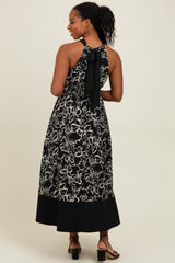 woman wearing a black floral print halter maxi dress with a tie back and a contrasting black hem