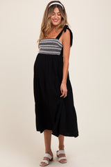 woman wearing a black maternity dress with embroidered bodice and tie straps, showcasing her baby bump