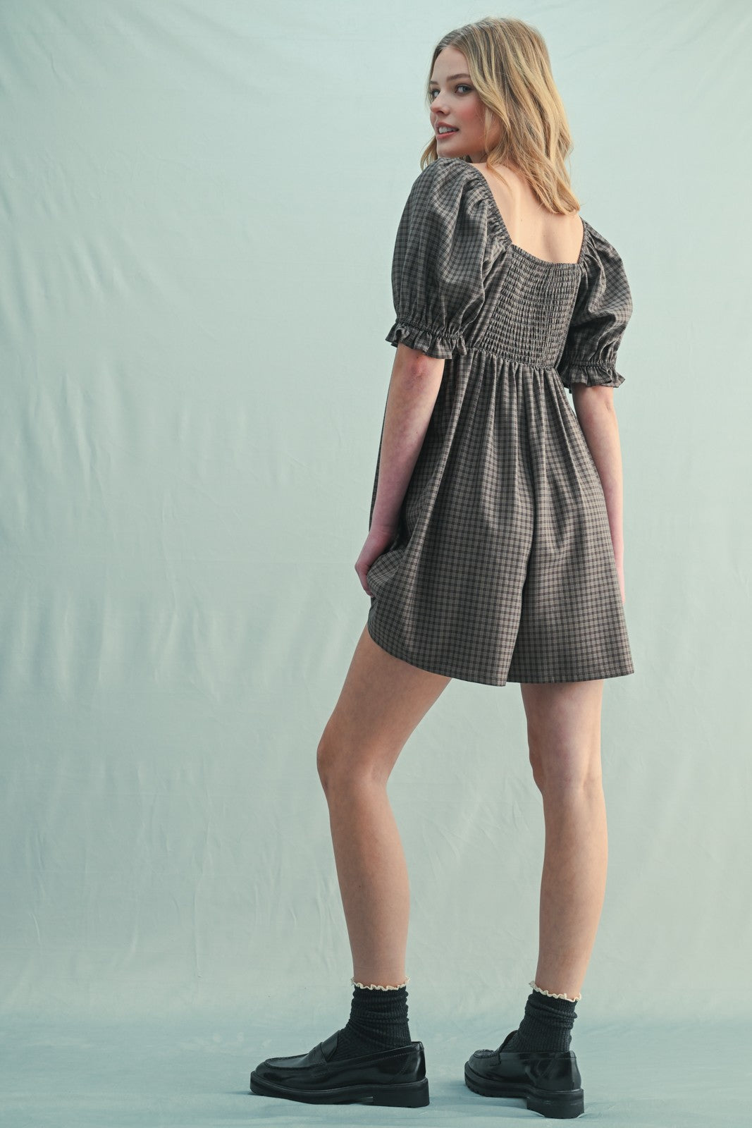 woman wearing a brown checkered puff sleeve romper with a square back and paired with black ankle boots