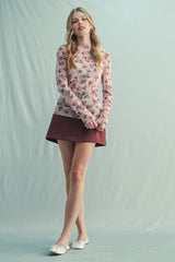 woman wearing a floral long sleeve top with a maroon suede mini skirt and white flats