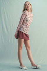 woman wearing a long sleeve floral top in pink and a maroon mini skirt with white flats