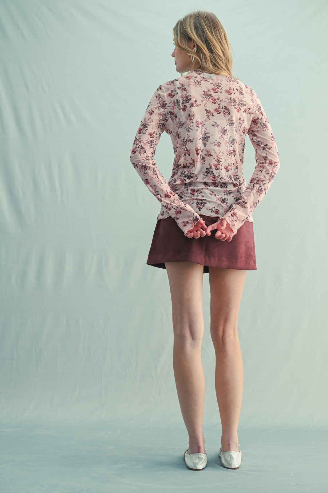 woman wearing a light pink floral long sleeve top and a brown suede mini skirt, viewed from the back