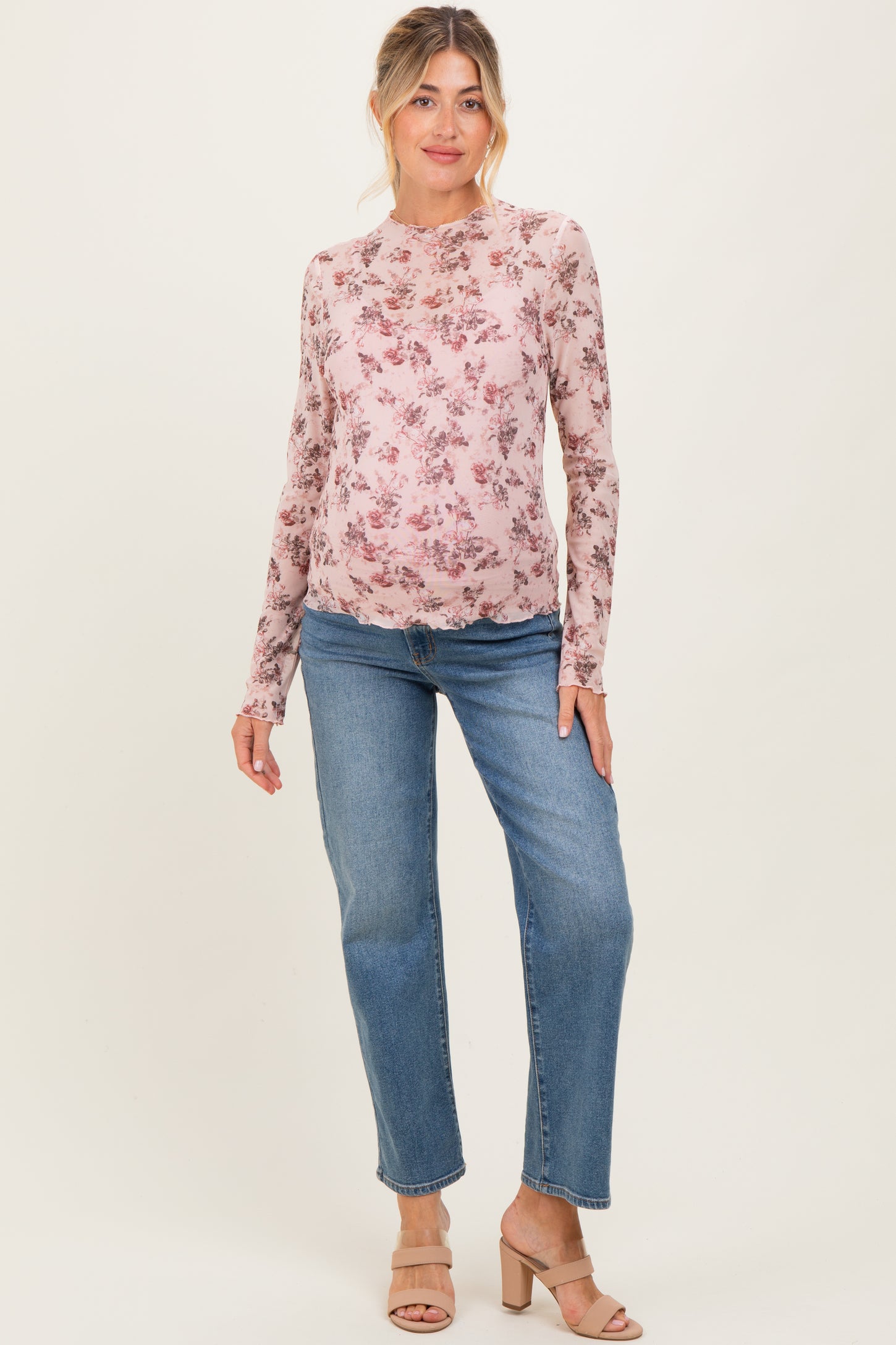 woman wearing a floral long sleeve maternity top with a round neckline and light blue straight leg jeans, showing her baby bump