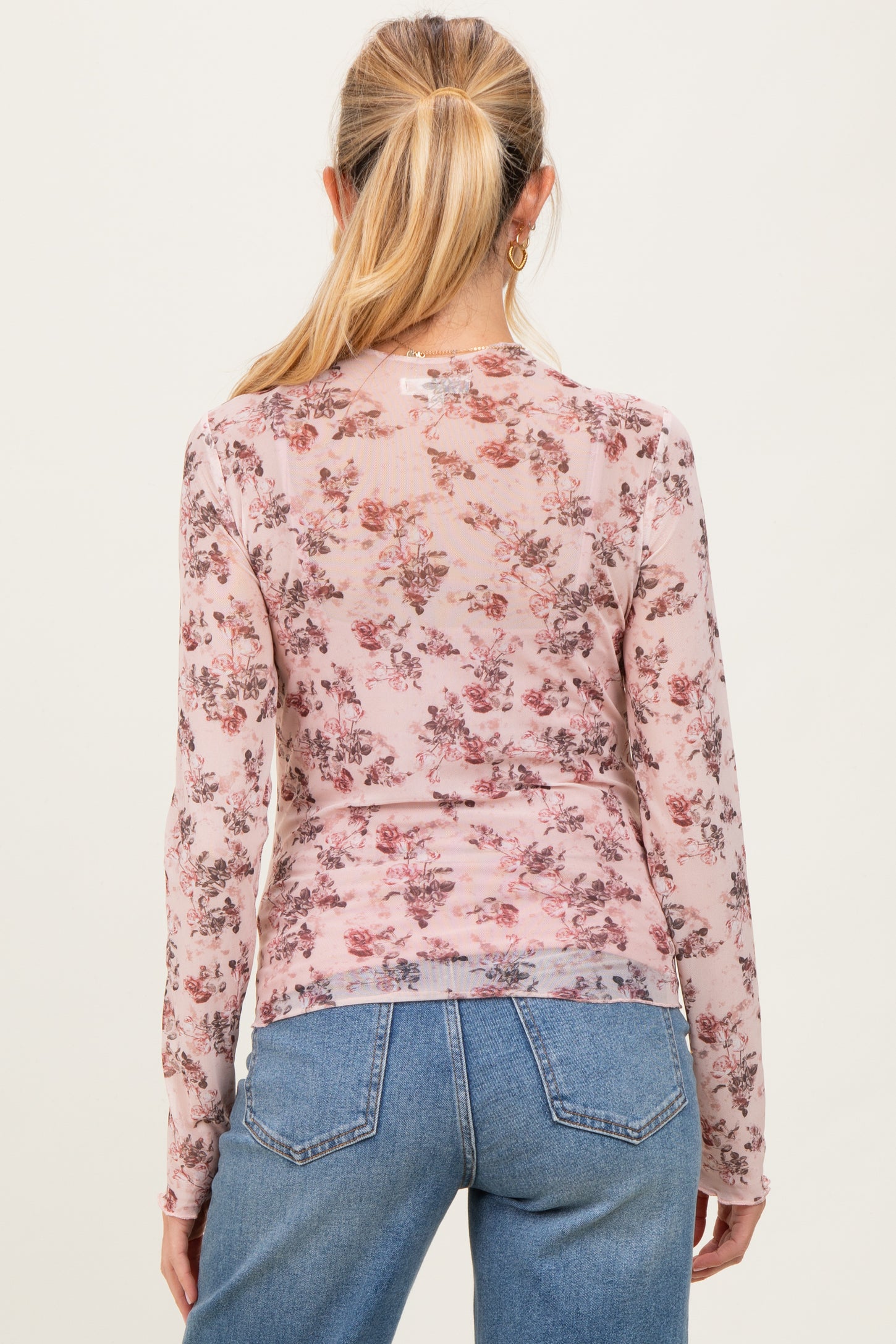 woman wearing a sheer pink long sleeve maternity top with floral print, showing her back and styling with high-waisted jeans