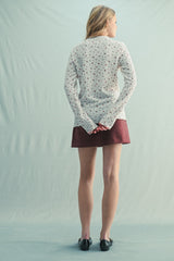 woman wearing a cream floral long sleeve sweater with a maroon skirt, viewed from the back