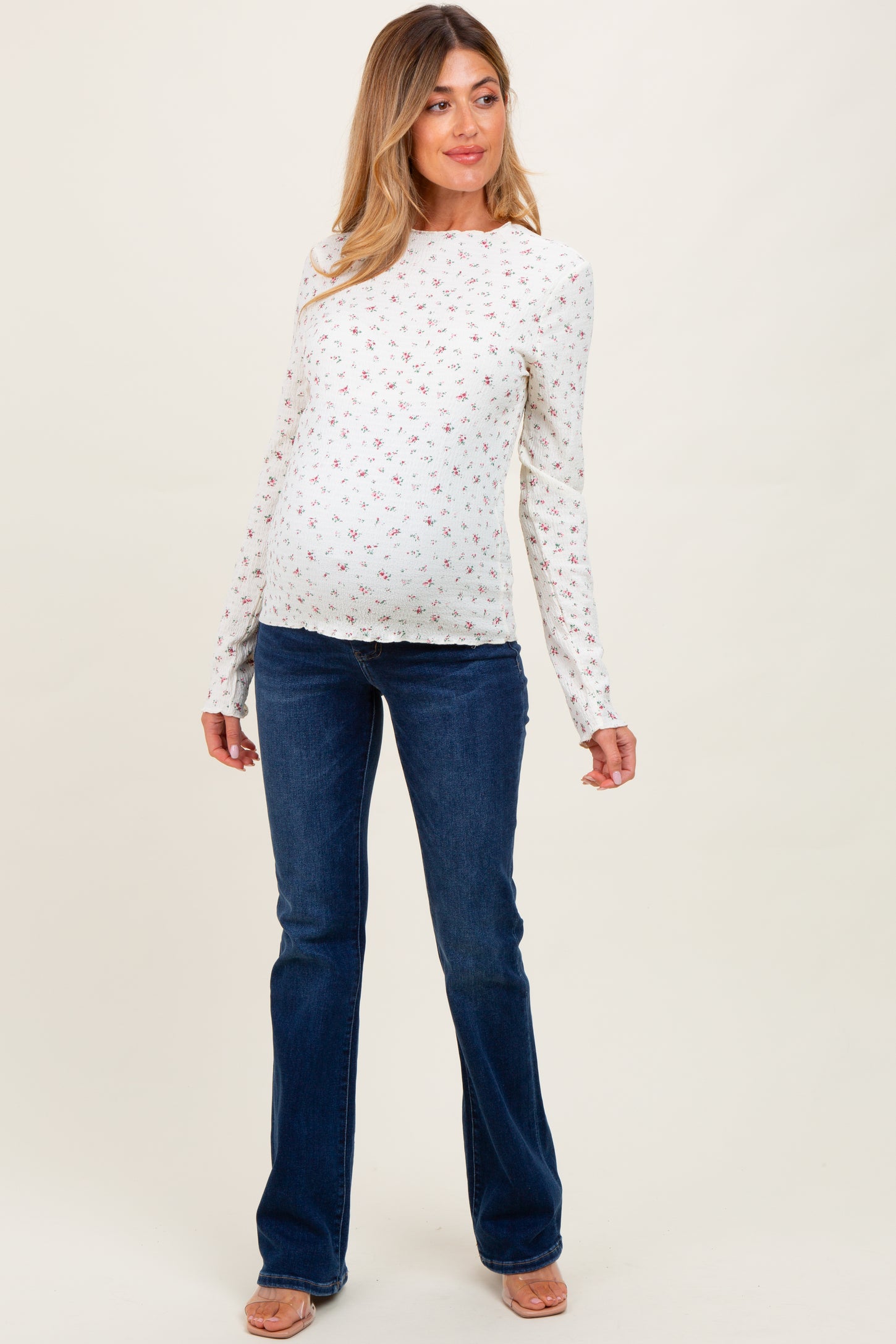 woman wearing a white floral long sleeve maternity top and blue flared jeans, showcasing her baby bump