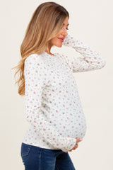 woman wearing a light blue maternity sweater with floral patterns and holding her baby bump