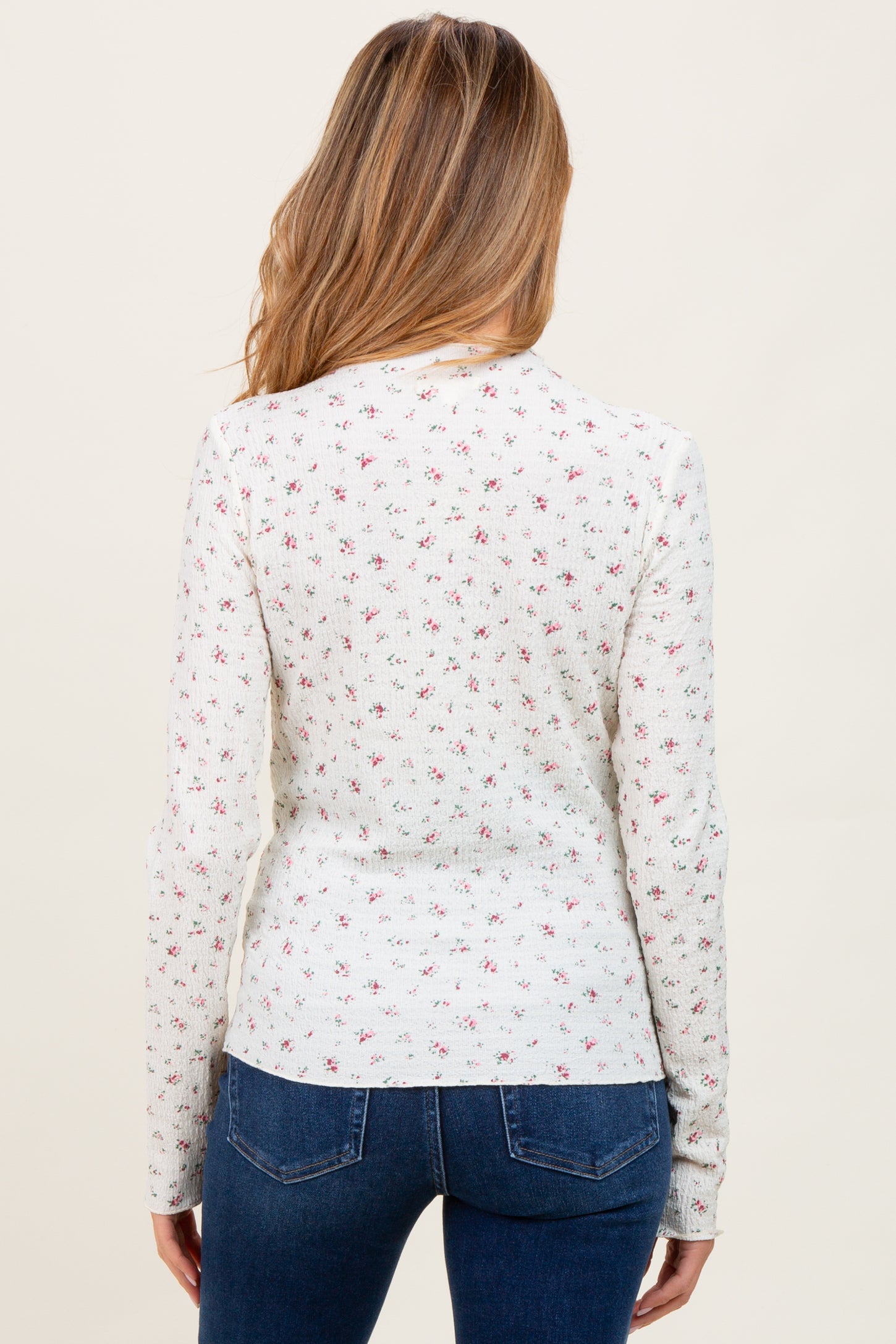 woman wearing a white long sleeve maternity top with a floral pattern and on-trend round hem, viewed from the back