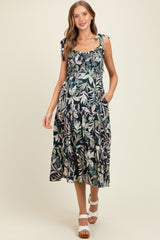 woman wearing a dark floral print maternity dress with tie shoulder straps and pockets, showing her baby bump