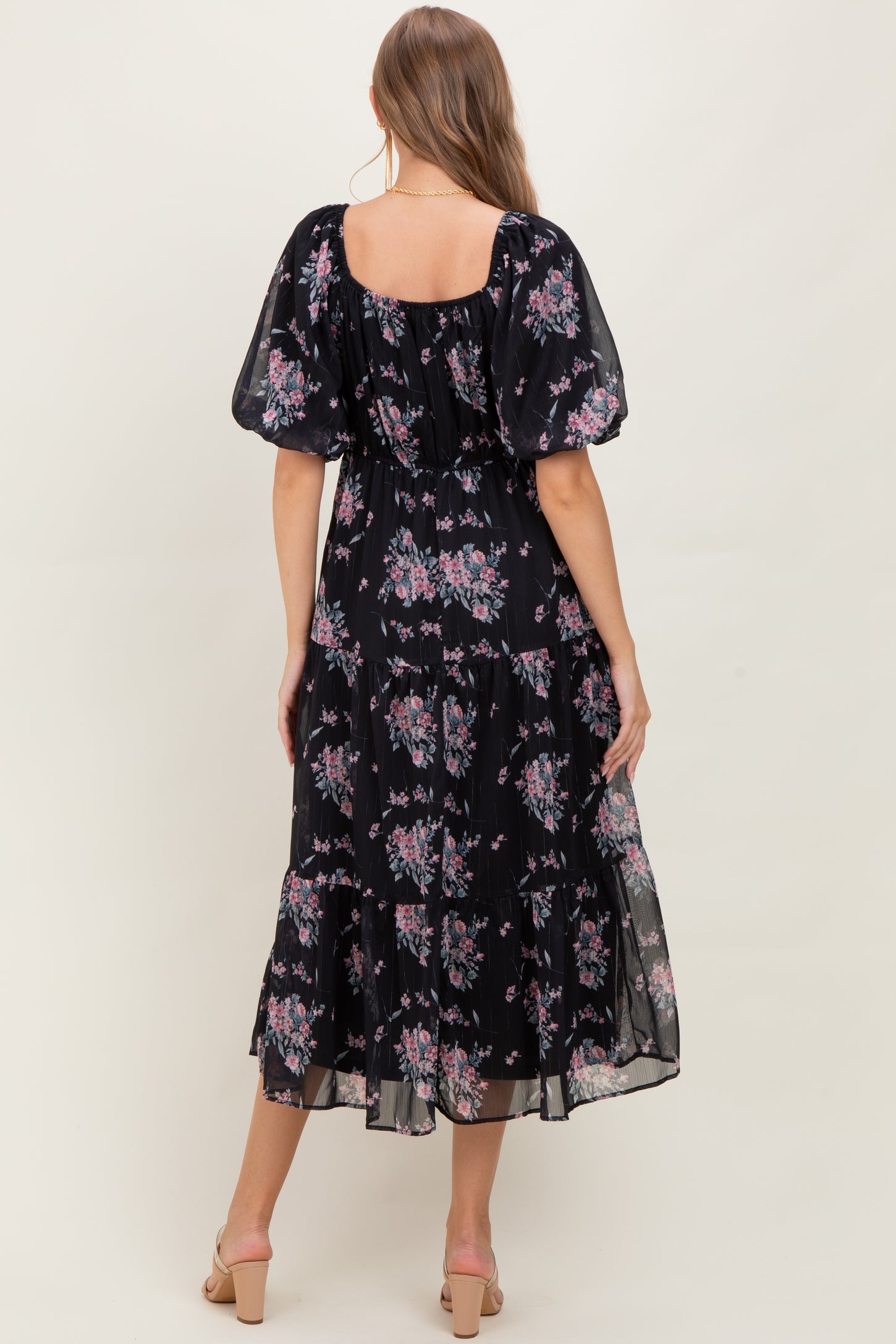 woman wearing a black floral maternity maxi dress with puff sleeves and a tiered skirt, showing a baby bump