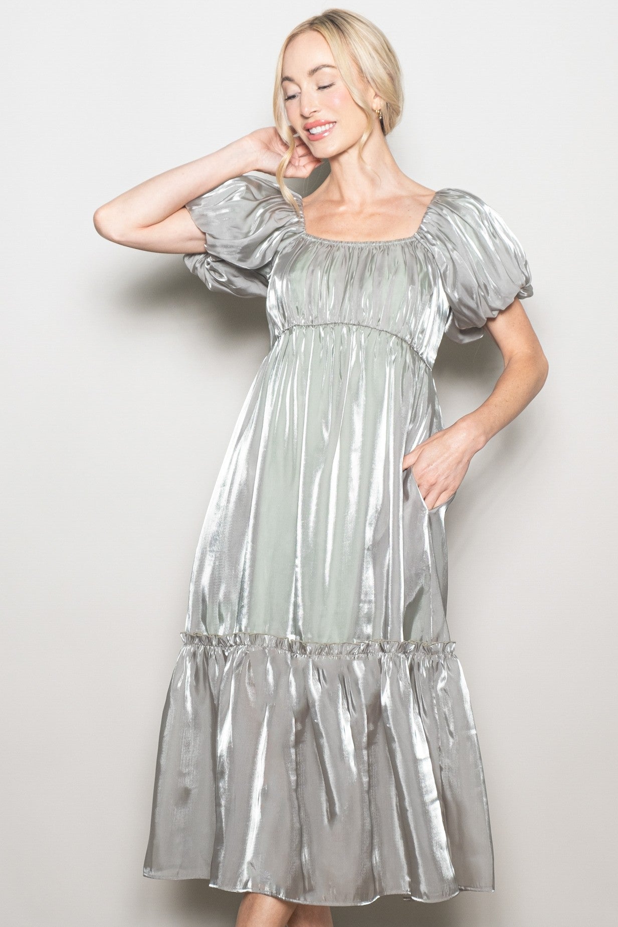 woman wearing a silver satin midi dress with puff sleeves and a tiered skirt, posing with one hand on her hip
