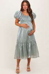 woman wearing a pale green satin maternity dress with puff sleeves and a tiered skirt, displaying her baby bump