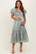woman wearing a pale green satin maternity dress with puff sleeves and a tiered skirt, displaying her baby bump