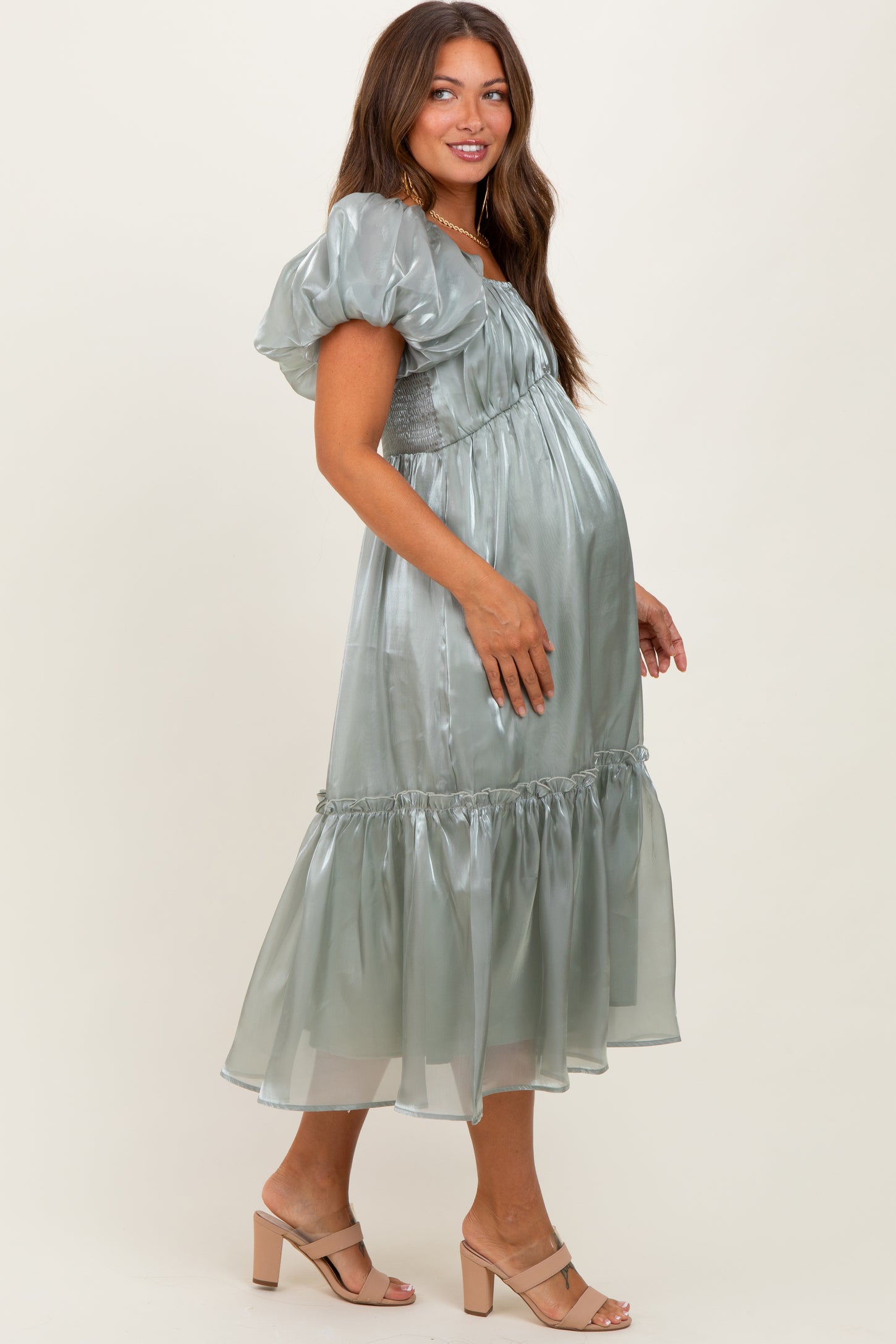 woman wearing a light green maternity dress with puff sleeves and a tiered skirt, showing her baby bump