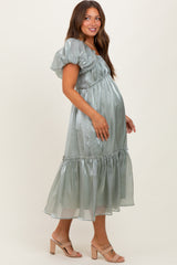 woman wearing a light green maternity dress with puff sleeves and a tiered skirt, showing her baby bump