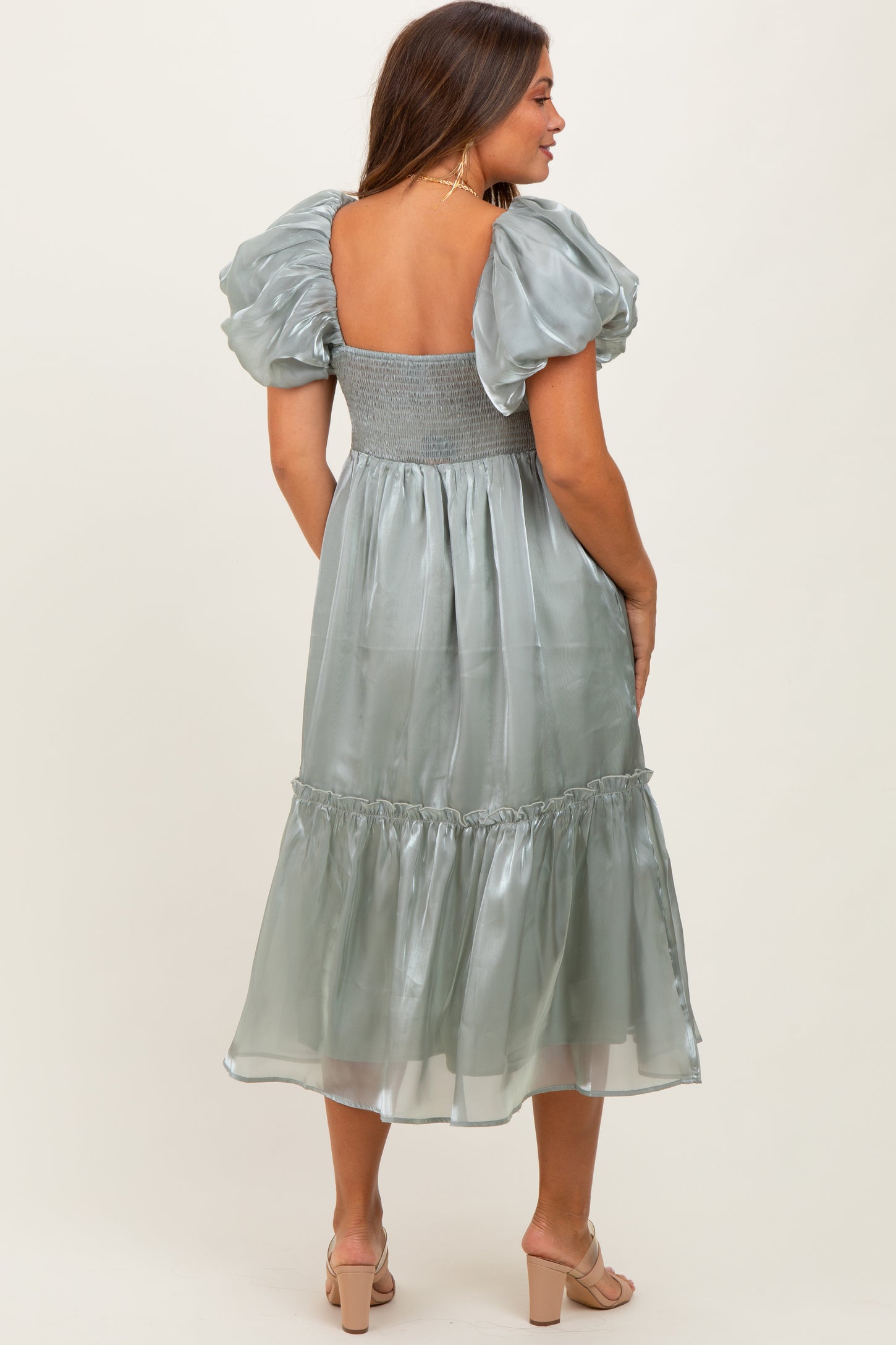 woman wearing a backless silver green maternity dress with puff sleeves and a tiered skirt