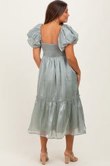 woman wearing a backless silver green maternity dress with puff sleeves and a tiered skirt