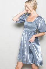 woman wearing a shimmery light blue short puff sleeve dress with a square neckline and smocked bodice