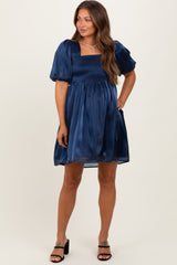 woman wearing a navy blue short puff sleeve maternity dress with a smocked bodice and flowing skirt, holding her baby bump