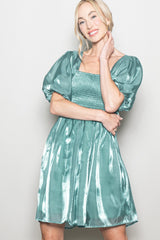 woman wearing a teal puff sleeve mini dress with a smocked bodice and a shiny finish