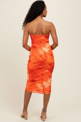 woman wearing an orange floral strapless midi dress with a form-fitting silhouette and a back zipper detail