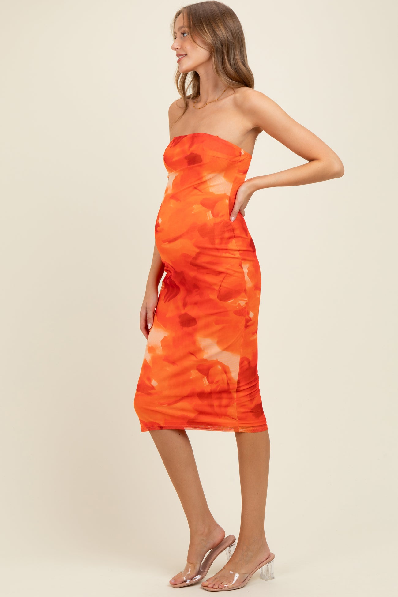woman wearing a strapless orange floral maternity dress that shows off her baby bump