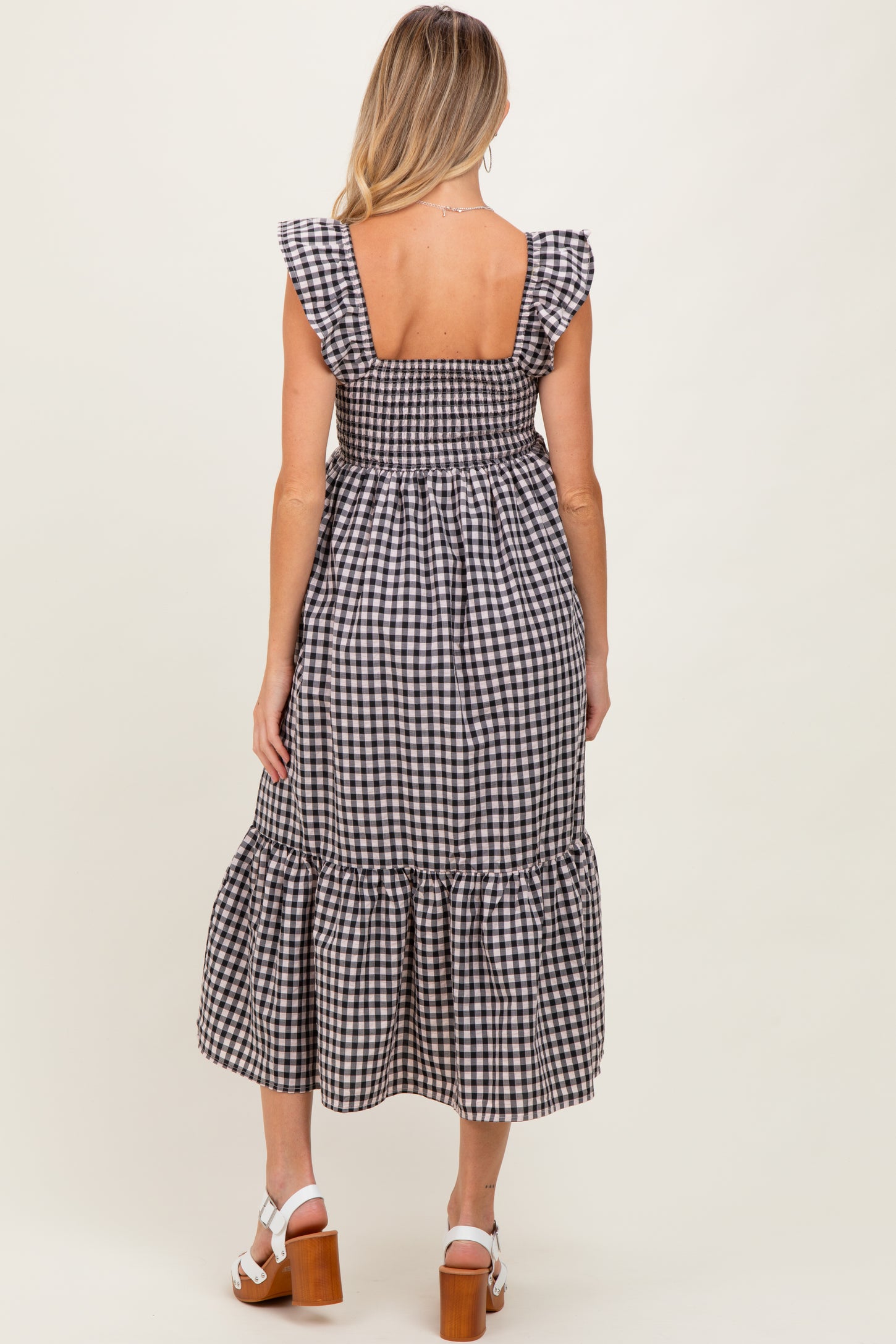 woman wearing a black and white gingham maternity dress with ruffle sleeves and a tiered hemline, showing a baby bump