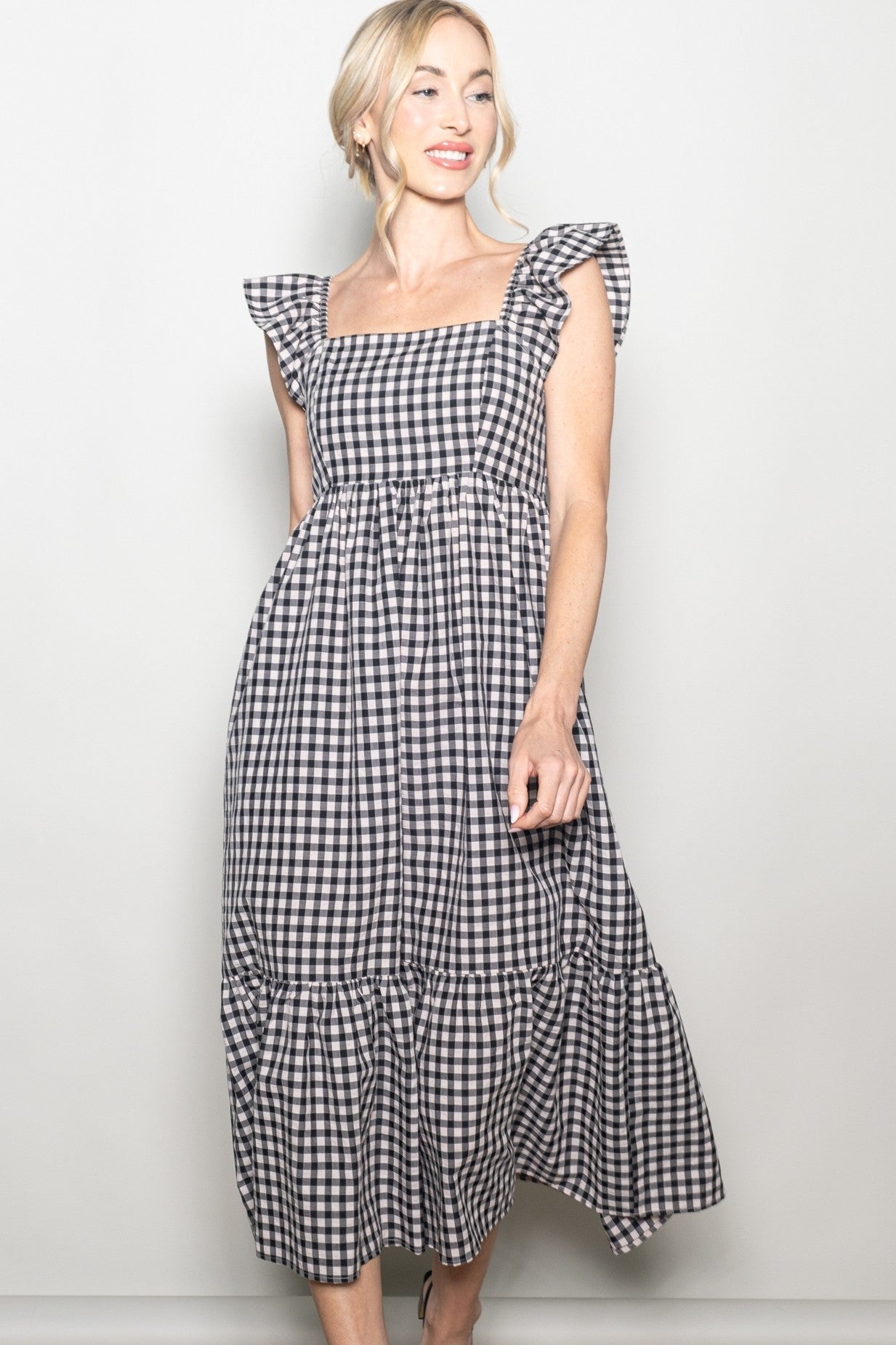 woman wearing a black and white gingham maxi dress with ruffle sleeves and a tiered skirt