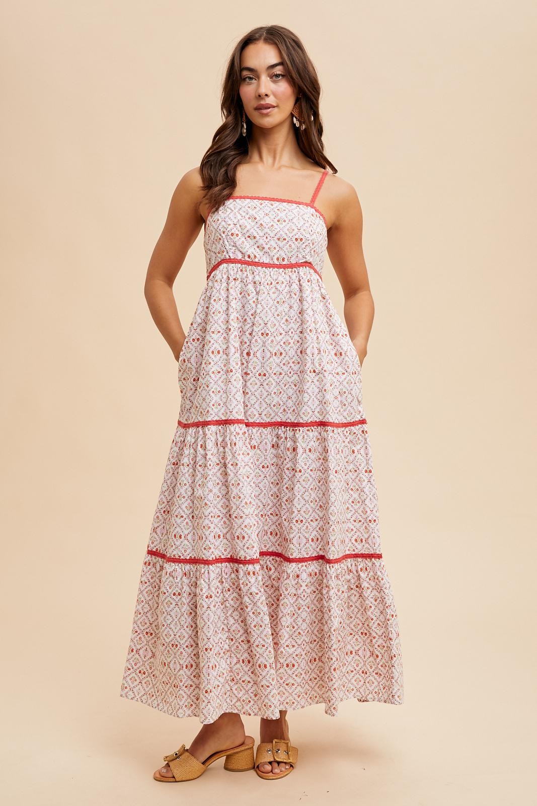 woman wearing a white maxi dress with patterned detailing and red trim, featuring adjustable straps and pockets