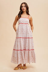 woman wearing a white maxi dress with patterned detailing and red trim, featuring adjustable straps and pockets
