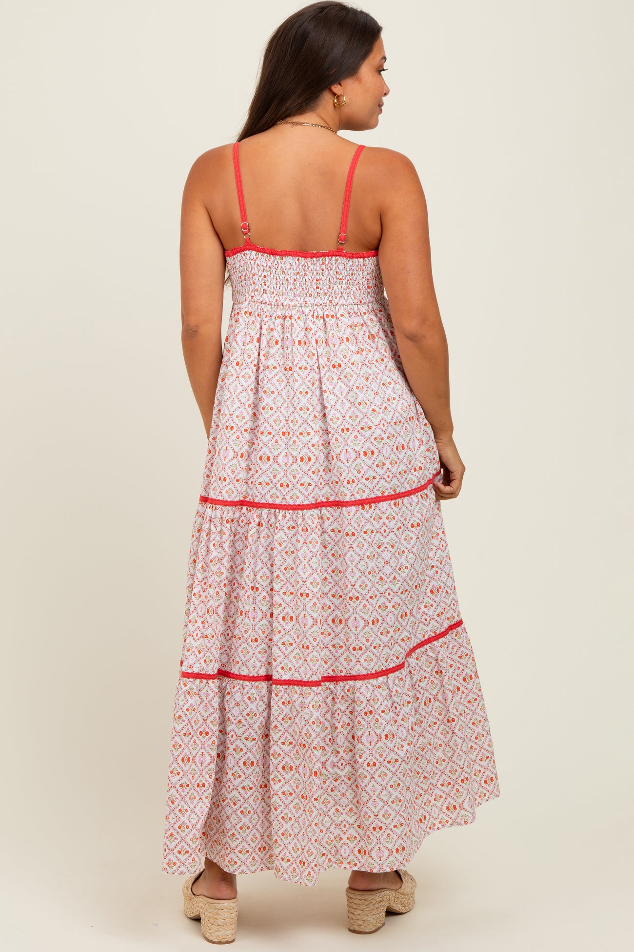 woman wearing a patterned white and pink maternity maxi dress with smocked back and tiered skirt, showing her baby bump