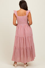 woman wearing a pink and white gingham maternity maxi dress with ruffled straps and a smocked bodice