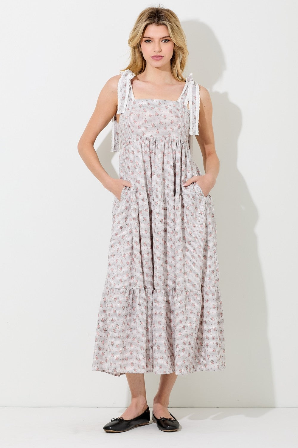 woman wearing a light pink floral maxi dress with adjustable tie straps and pockets