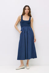 woman wearing a navy blue sleeveless maxi dress with a fitted bodice and gathered skirt, standing with hands in pockets