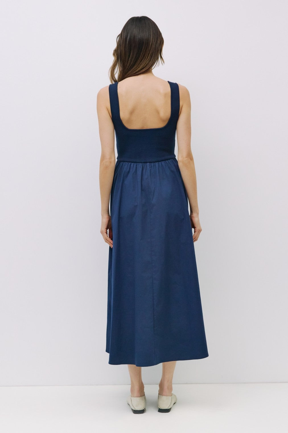 woman wearing a navy sleeveless maxi dress with a fitted bodice and a flared skirt, viewed from the back