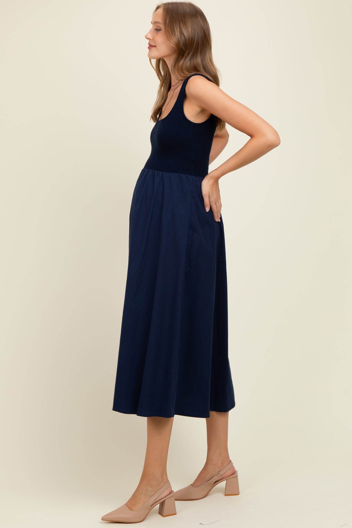 woman wearing a navy blue sleeveless maternity dress with a flowy skirt and visible baby bump
